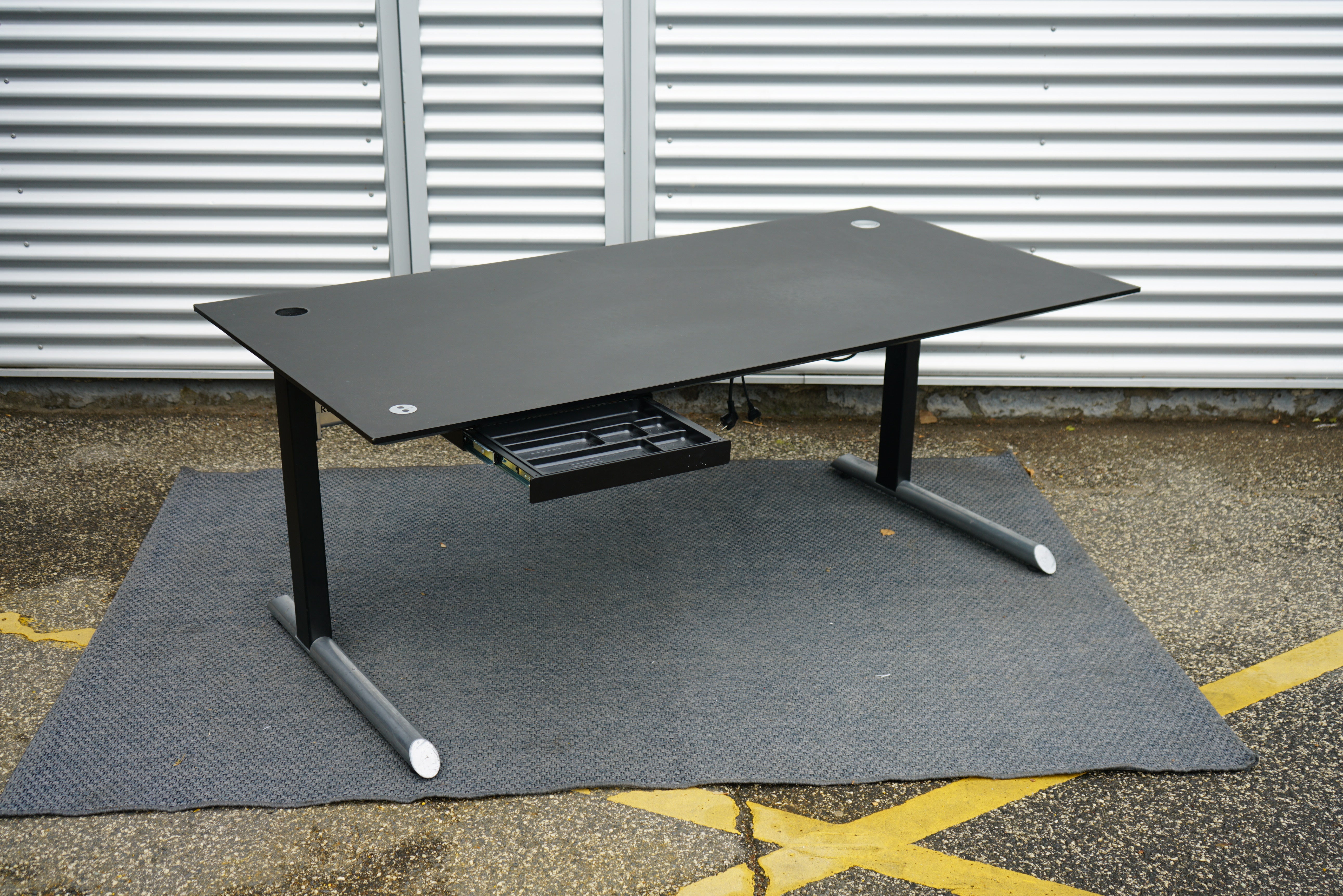 Rumas hæve-sænkebord i sort linoleum 180x90 cm med skuffe og stikkontakt set fra skrå vinkel